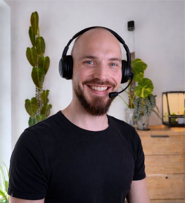 Man wearing a headset in an indoor setting with plants and a desk.