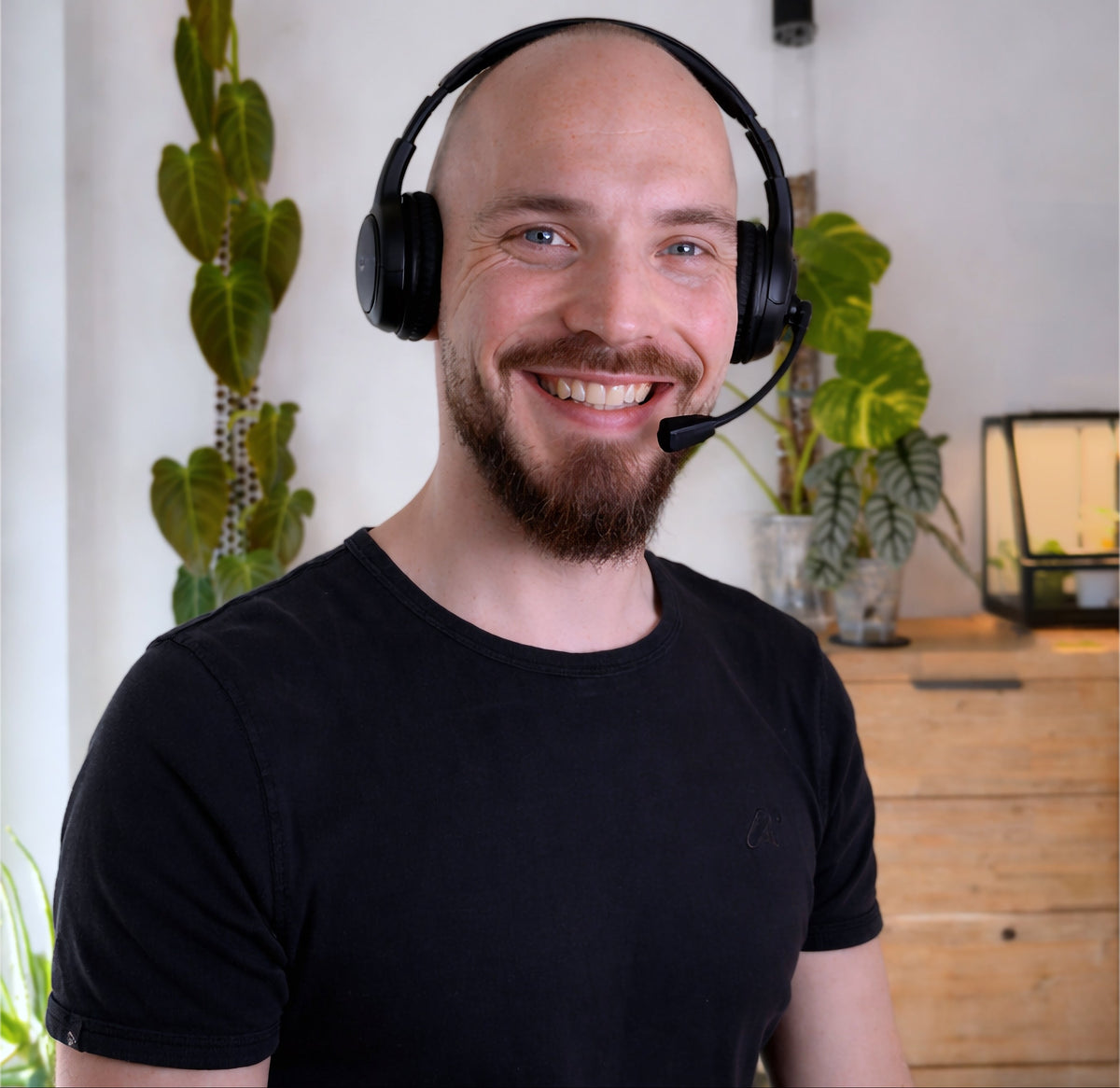 Man wearing a headset in an indoor setting with plants and a desk.